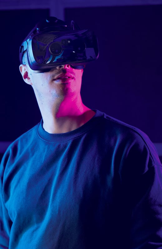 A person wears a VR headset and stands in a room with purple and blue ambient light.